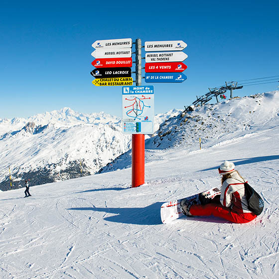 Snowboarder sitting next to Les Menuires sign